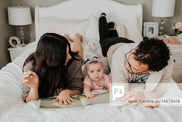 Couple reading with baby daughter on bed in bedroom