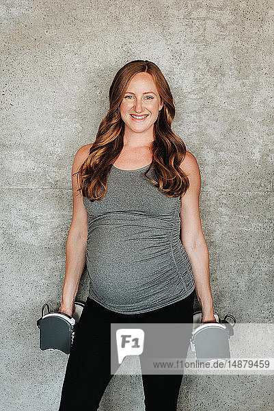 Schwangere Frau mit Gewichten neben Betonwand