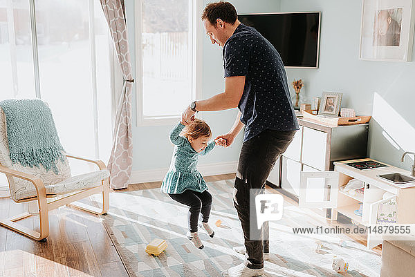 Father playing with toddler daughter on living room rug