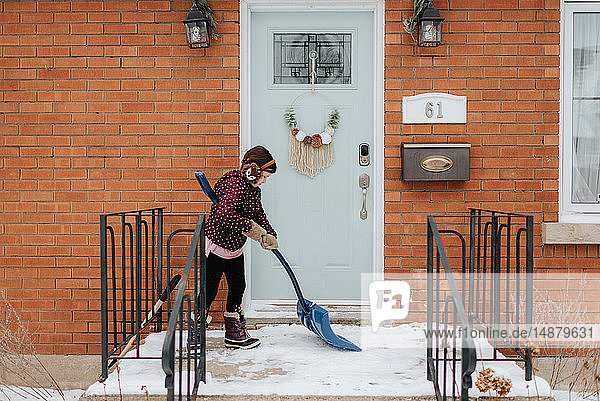 Girl shovelling snow on porch