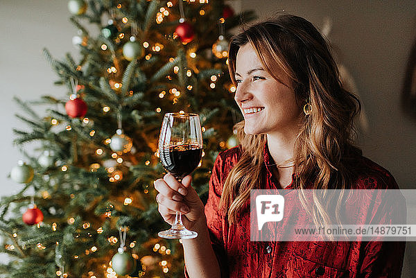 Frau trinkt Wein neben geschmücktem Weihnachtsbaum