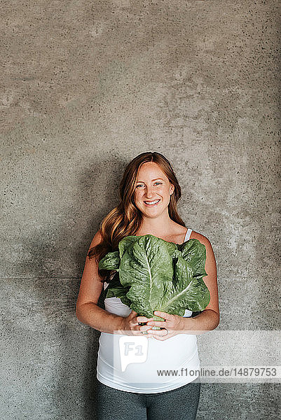 Pregnant woman holding up lettuce