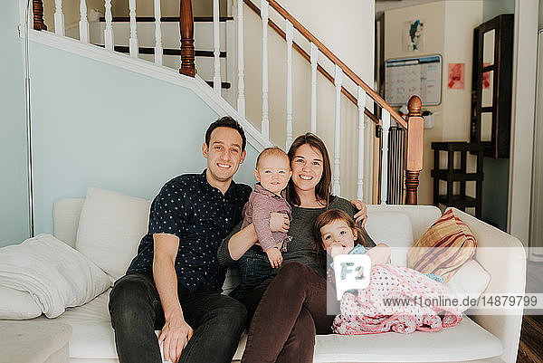 Mittelgroßes erwachsenes Paar auf dem Sofa mit Baby-Sohn und Kleinkind-Tochter  Porträt