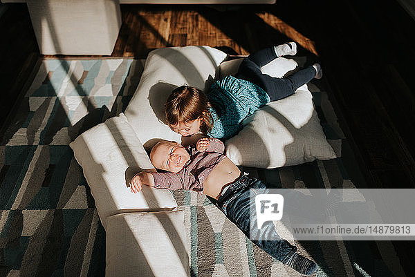 Kleiner Junge und kleine Schwester liegen auf Kissen auf dem Wohnzimmerboden  Blick von oben