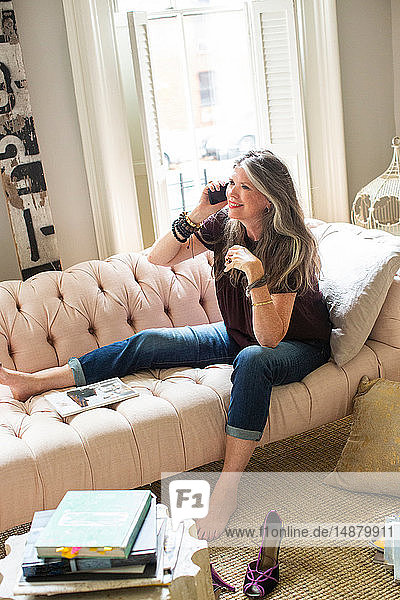 Stylish mature woman sitting on sofa making smartphone call