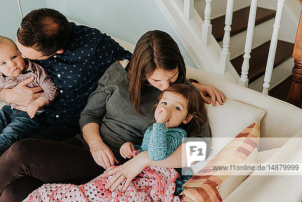 Mittelgroßes erwachsenes Paar auf dem Sofa mit Baby-Sohn und Kleinkind-Tochter