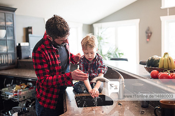 Vater beobachtet Sohn beim Händewaschen in Küchenspüle