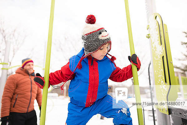 Junge mit Vater klettert auf Spielplatzrutsche im Schnee