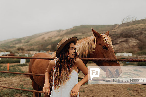 Junge Frau mit Filzhut lehnt neben Pferd am Zaun  Jalama  Kalifornien  USA