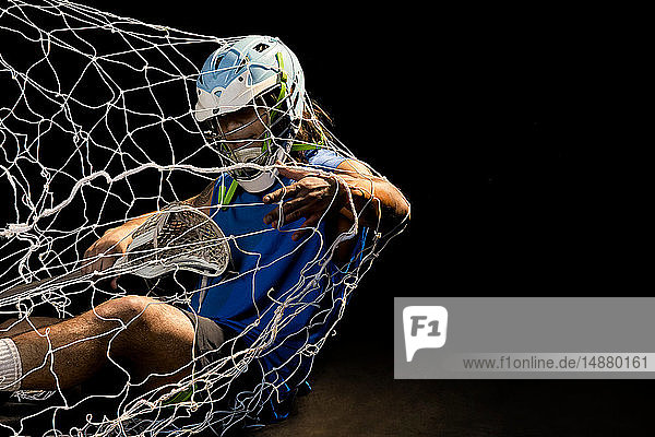 Junger männlicher Lacrosse-Spieler in Aktion  der ins Netz fällt  vor schwarzem Hintergrund