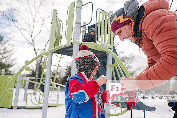 Father putting on boy's gloves by playground slide in snow