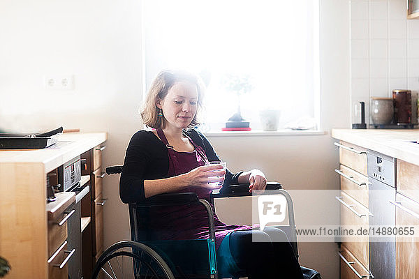 Frau im Rollstuhl mit einem Glas Wasser in der Küche