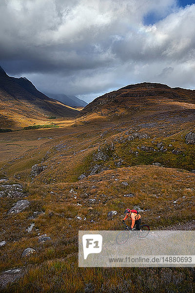 Männlicher Mountainbiker radelt auf Feldweg in Bergtal-Landschaft  erhöhte Ansicht  Achnasheen  Schottische Highlands  Schottland