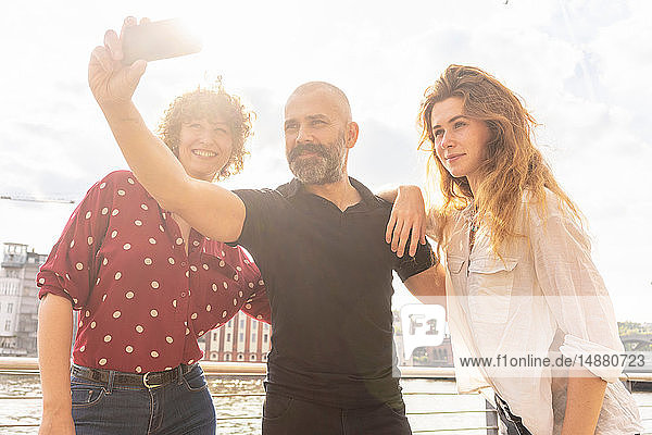 Mann und Freundinnen beim Selfie mit Smartphone auf der Brücke