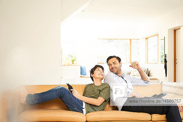 Junge und Vater benutzen digitale Tabletts Rücken an Rücken auf dem Sofa