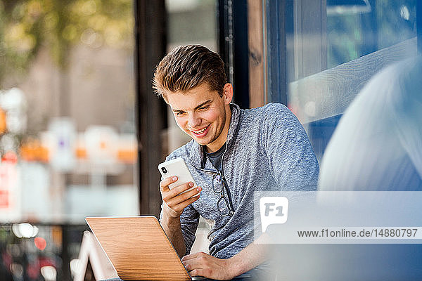 Junger Mann benutzt Smartphone und Laptop im Café