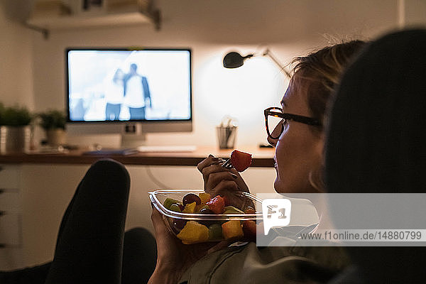 Woman relaxing in front of TV with fruit salad