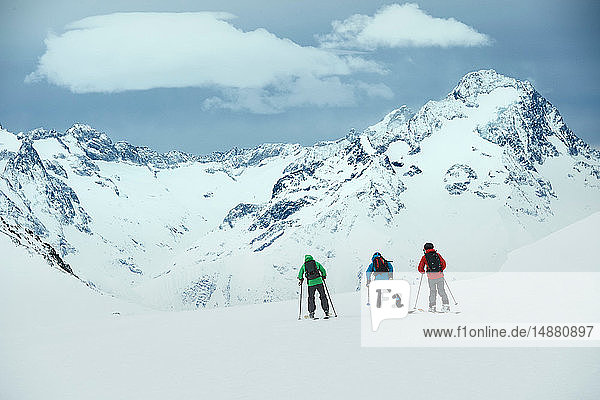 Landschaft mit drei männlichen Skifahrern  die in Richtung Berg fahren  Rückansicht  Alpe-d'Huez  Rhône-Alpes  Frankreich