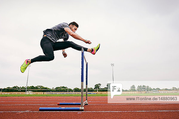 Athlet springt über Hürde auf Laufbahn