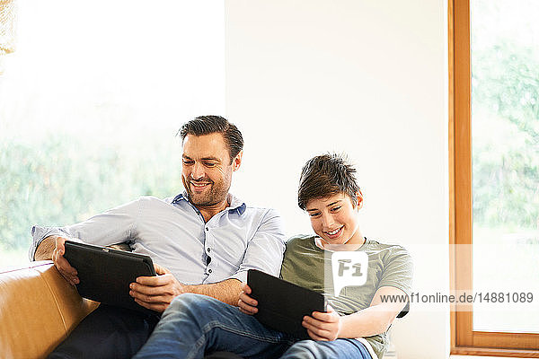 Junge und Vater schauen auf digitale Tabletts  während sie auf dem Sofa liegen
