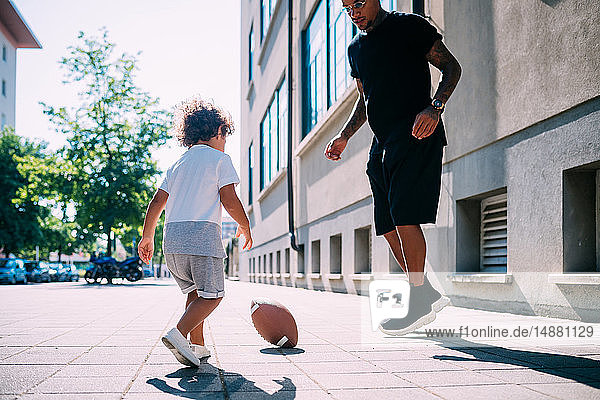 Father and son playing with rugby ball on sidewalk