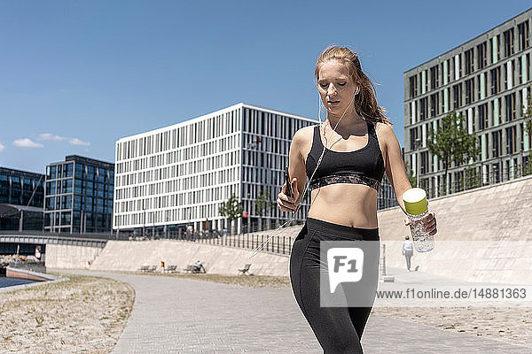 Young woman running and using smartphone in city  Berlin  Germany