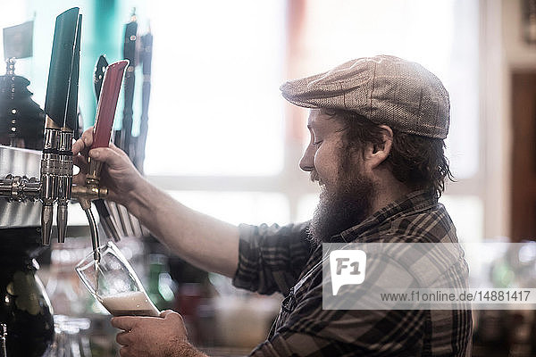 Barman pouring beer from pump in traditional Irish public house