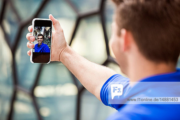 Young man taking selfie in front of glass wall  London  UK