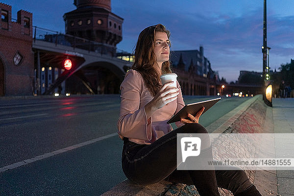 Junge Frau hält heißes Getränk in der Hand und benutzt ein digitales Tablett auf der Brücke  Berlin  Deutschland
