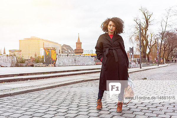 Mittelgroße erwachsene Frau in schickem Mantel auf gepflasterter Straße  Berlin  Deutschland