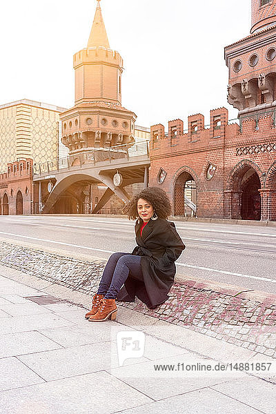 Mid adult woman in stylish coat sitting on Oberbaum Bridge  portrait  Berlin  Germany