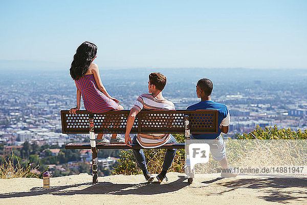 Drei junge erwachsene Freunde schauen von der Hügelbank aus auf das Stadtbild  Rückansicht  Los Angeles  Kalifornien  USA