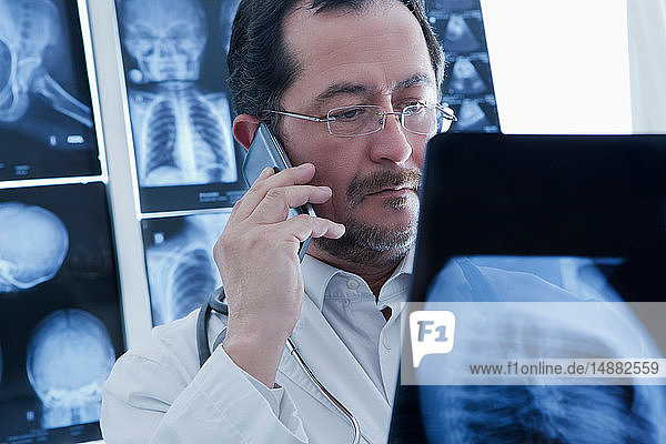 Arzt benutzt Smartphone und untersucht Röntgenbild