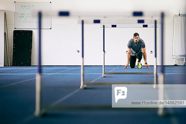 Sportler bereitet sich auf Hürden auf der Indoor-Laufbahn vor