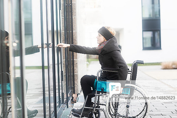 Woman in wheelchair opening door to building
