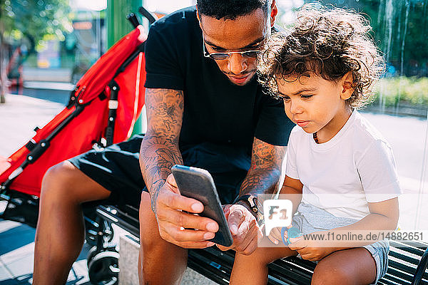 Father teaching son use smartphone on bench