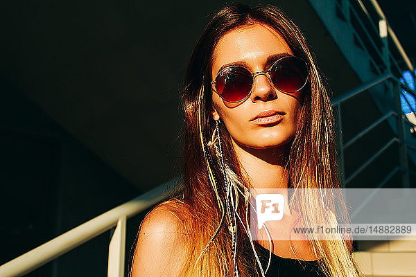 Junge Frau mit langen braunen Haaren und Sonnenbrille auf Treppen-  Kopf- und Schulterportrait