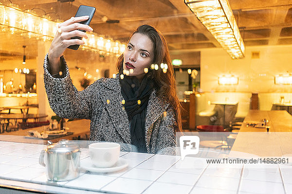Young woman taking selfie with smartphone in cafe  London  UK