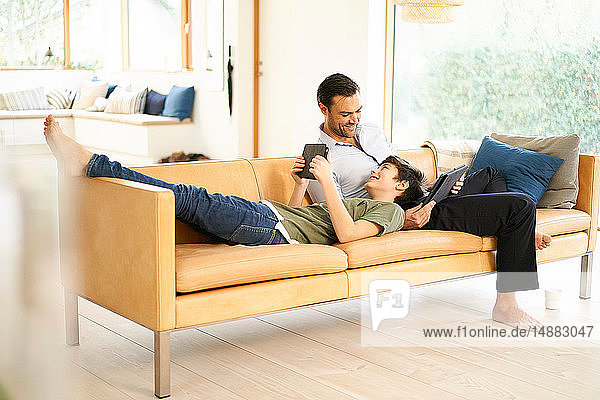 Junge und Vater benutzen digitale Tablets beim Entspannen auf dem Sofa