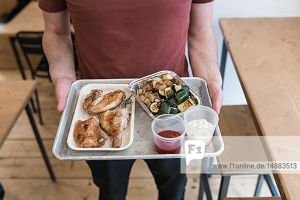 Customer with tray of grilled chicken vegetables and dipping sauce in restaurant
