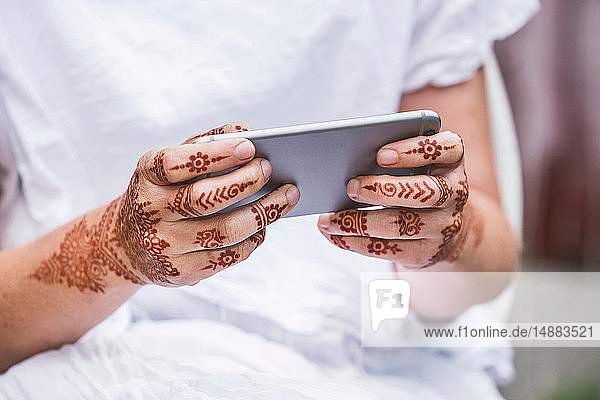Woman with henna tattoo on hands using smartphone