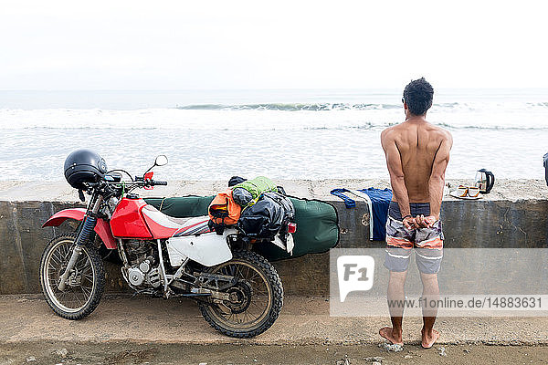 Surfer by motorbike stretching by sea wall  Pagudpud  Ilocos Norte  Philippines