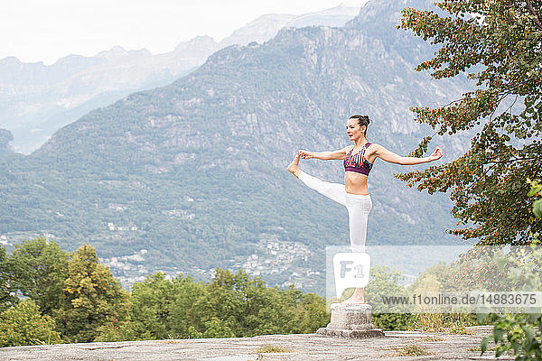 Woman practicing yoga  balancing on one leg on top of plinth  mountain landscape  Domodossola  Piemonte  Italy