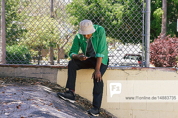 Junger Mann betrachtet Smartphone am Parkzaun  Los Angeles  Kalifornien  USA
