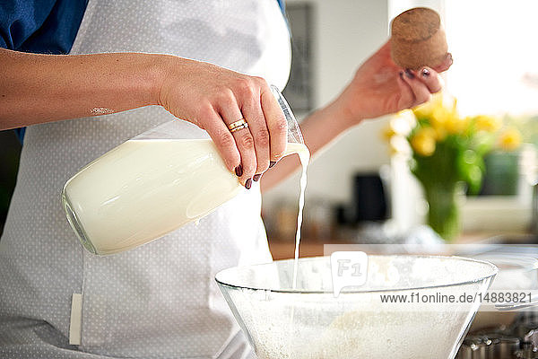 Frau gießt in Küche Milch in Rührschüssel