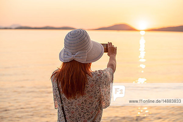 Tourist taking photograph of sunset on beach