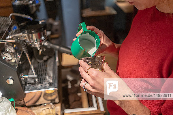 Weibliche Barista gießt geschäumte Milch in Kaffeeglas  abgeschnitten