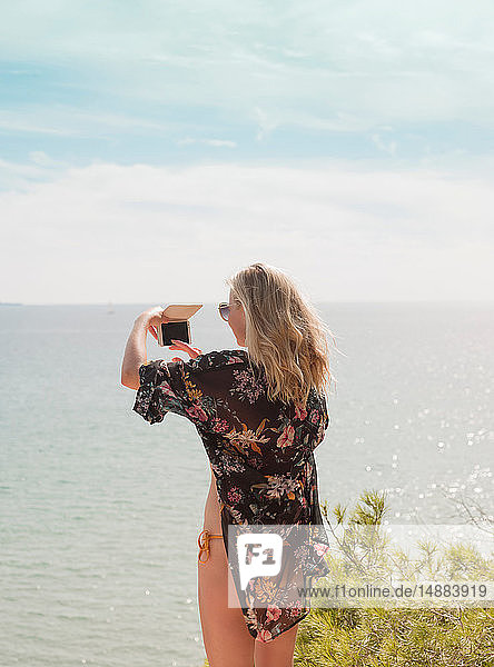 Frau fotografiert Meer an einem sonnigen Tag