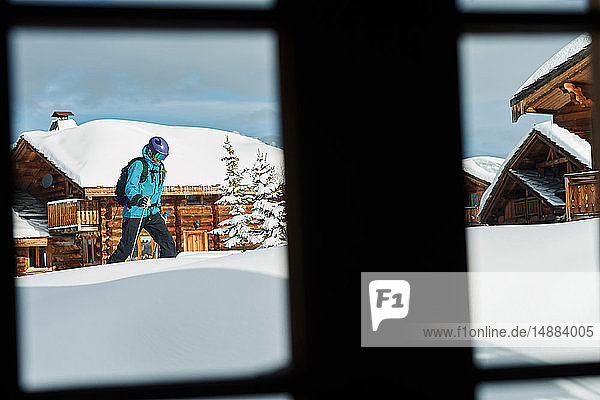 Fensteransicht eines männlichen Skifahrers  der durch Tiefschnee in der Nähe von Blockhütten läuft  Alpe-d'Huez  Rhône-Alpes  Frankreich