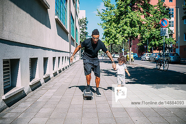 Father teaches son skateboarding on sidewalk